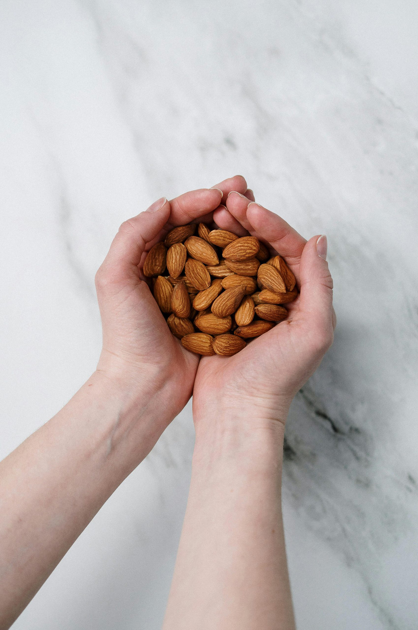 Hands holding almonds against a light, marbled background.