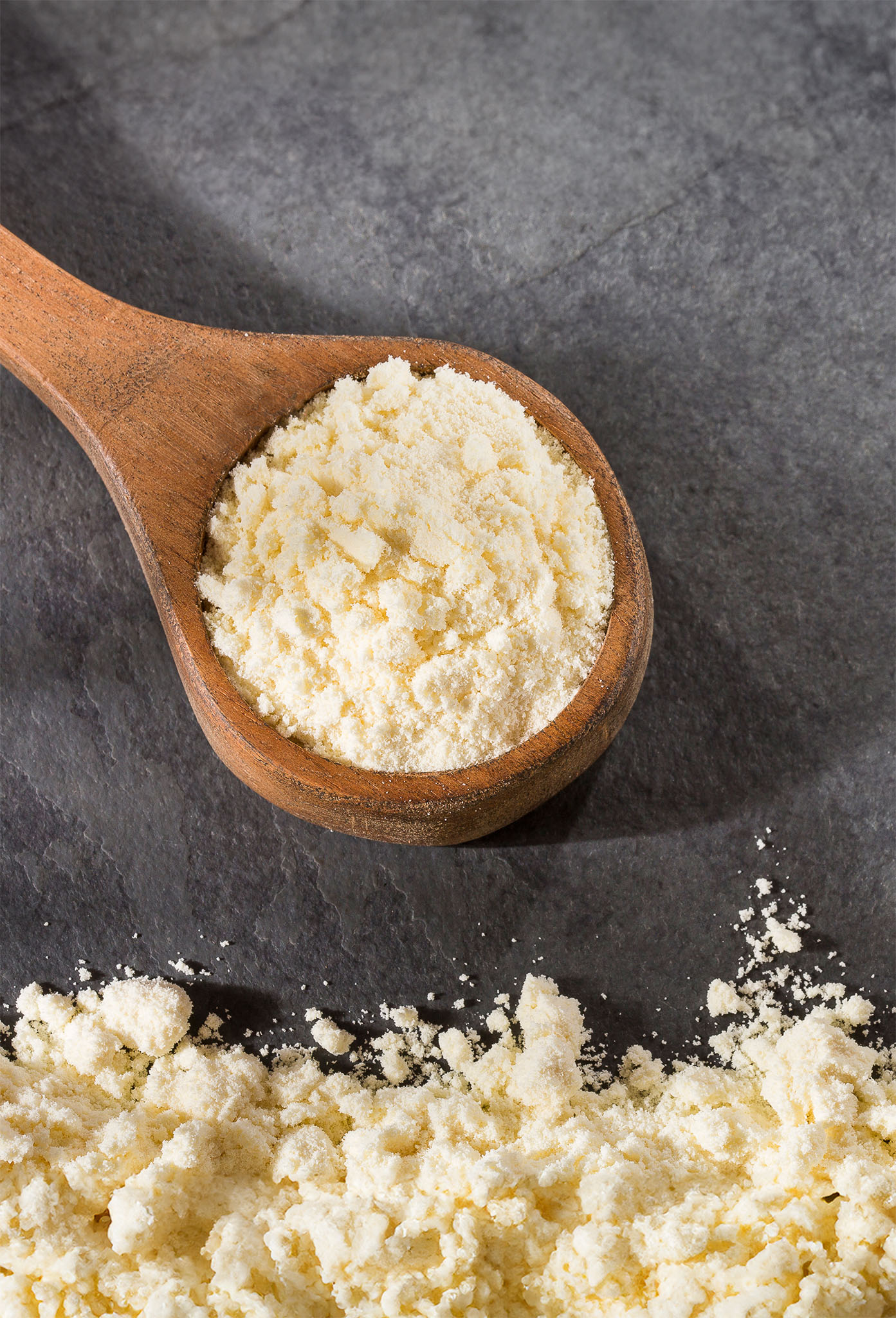 Milk powder in a wooden spoon, on a darker underground. 