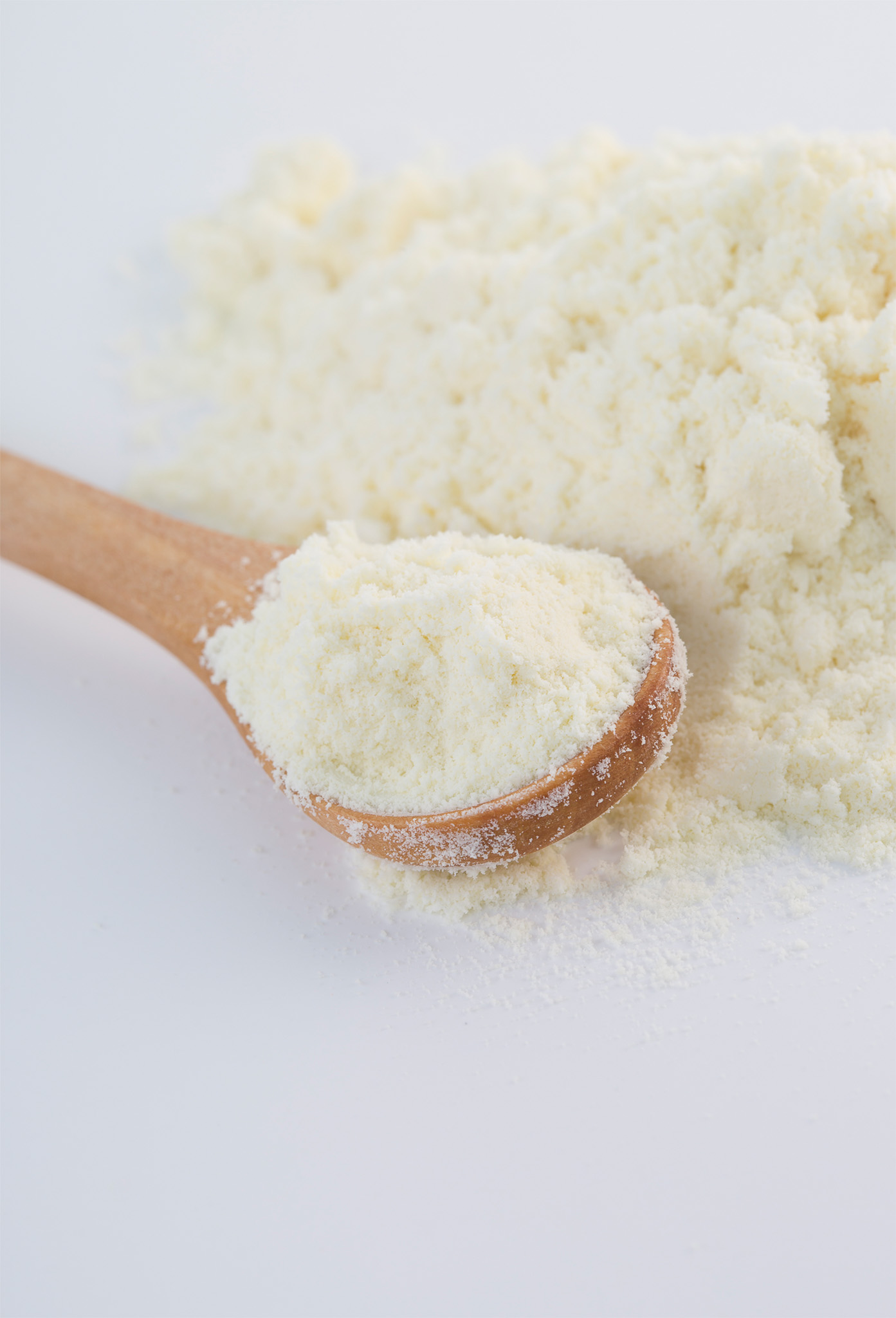 Molkenproteinpulver auf einem weißen Untergrund und auf einem Holzlöfel. 