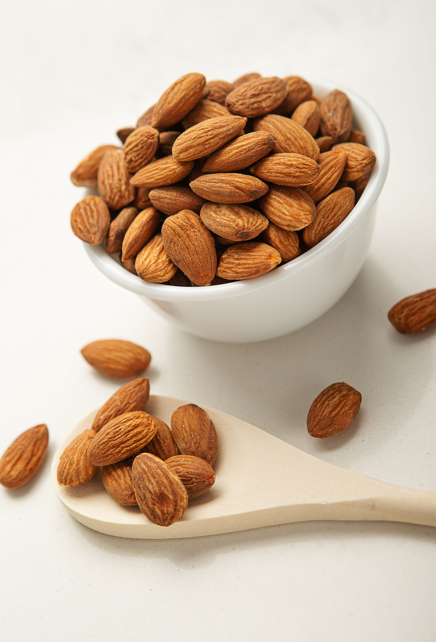Sweet almond kernels in a white bowl and wooden spoon filled with kernels.